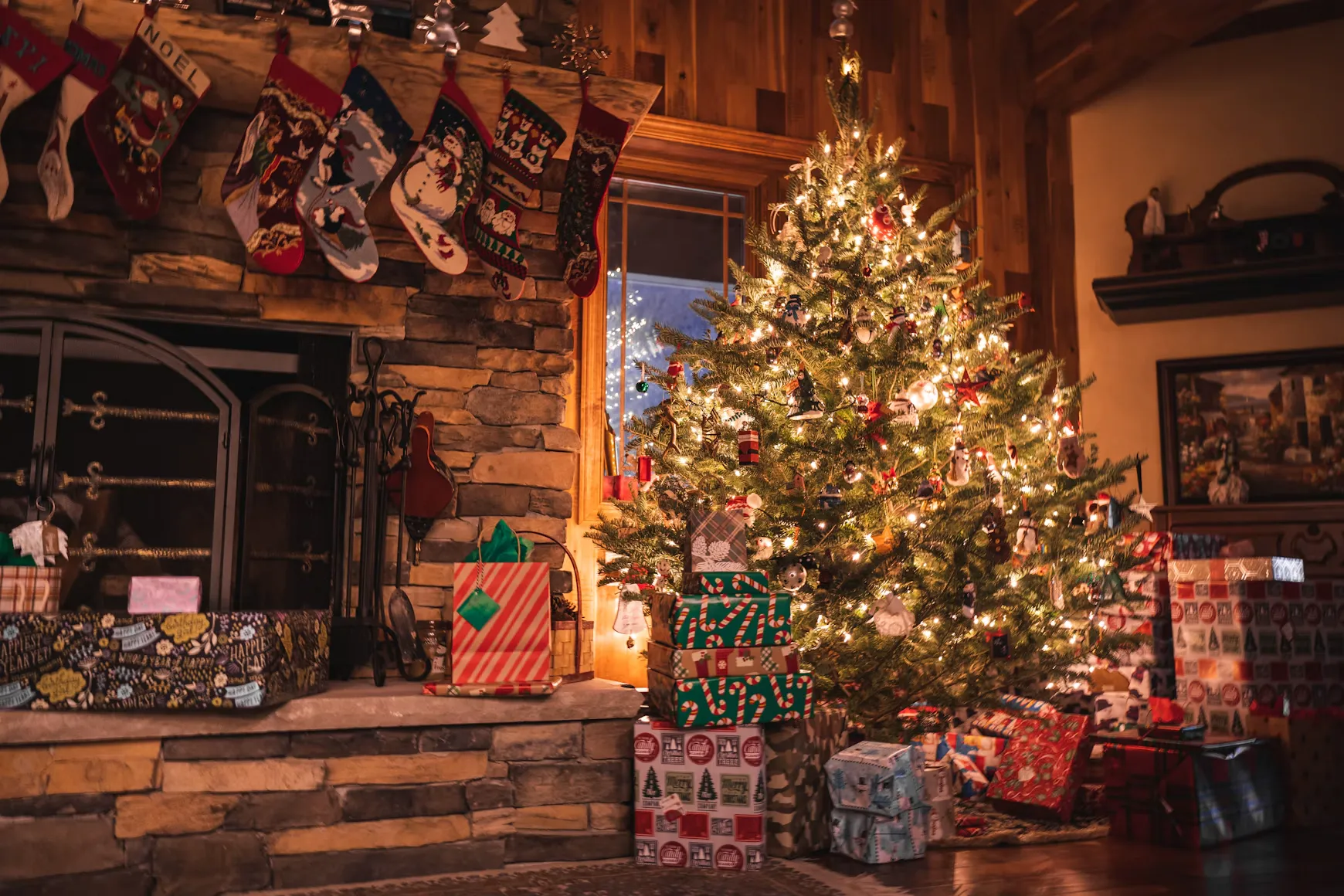 Gezellige woonkamer met verlichte kerstboom, cadeaus en kerstsokken bij de open haard